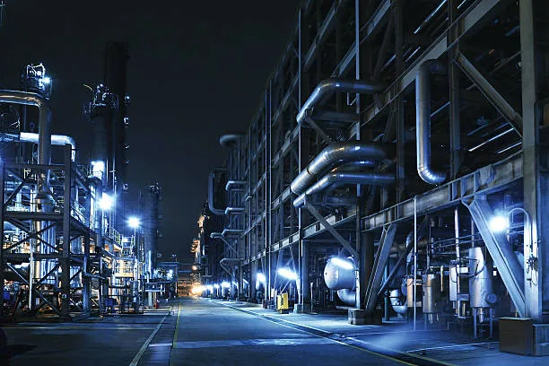 An illuminated access road between industrial pipe racks and equipment at night