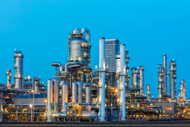 A row of refinery columns, platforms and pipework under a bright blue sky