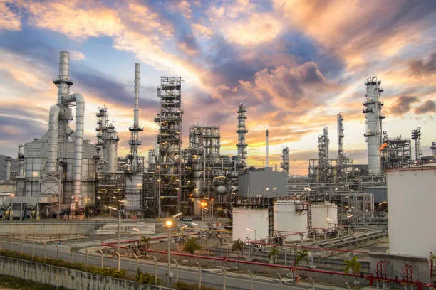 Tall refinery processing columns beneath blue and orange clouds