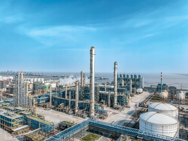 Wide view of refinery structures, a tall stack and cylindrical storage tanks under a blue sky