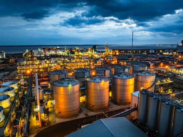 Cylindrical storage tanks and illuminated industrial equipment under a dark blue sky