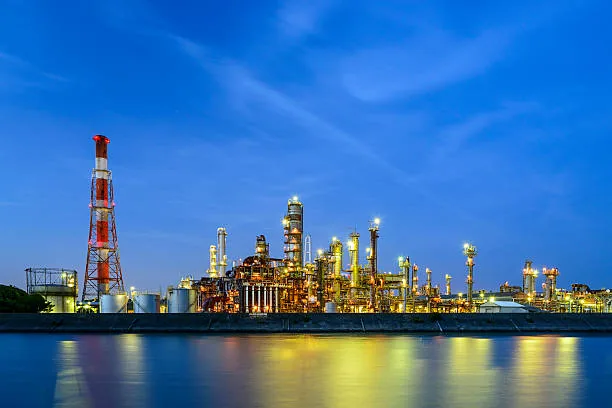 An illuminated industrial refinery reflected in calm water at twilight